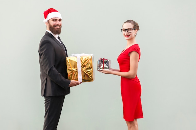 Couple regardant la caméra avec un sourire à pleines dents et s'offrent une boîte-cadeau en l'honneur de Noël