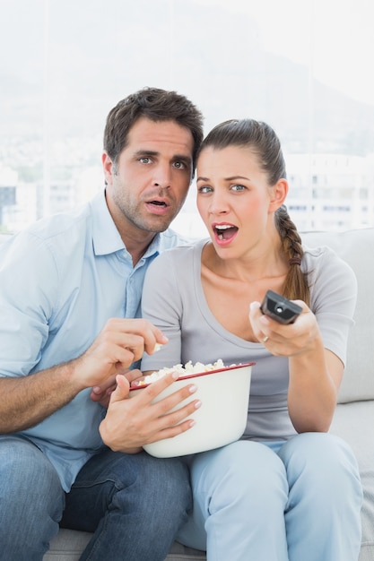 Couple, regarder un film effrayant sur le canapé avec un bol de maïs soufflé