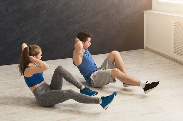 Couple de remise en forme faisant des craquements à l'intérieur. Jeune homme sportif et femme faisant des redressements assis sur un tapis. Mode de vie sain, gymnastique, concept de perte de poids