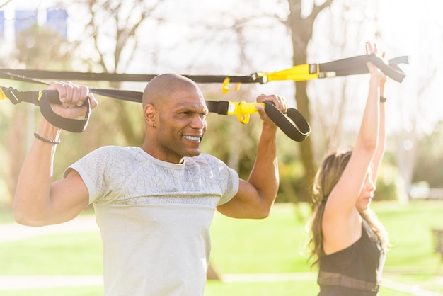 Couple de remise en forme faisant des exercices de bras et de biceps avec des sangles de remise en forme trx dans le parc. Personnes multiethniques exerçant à l'extérieur.