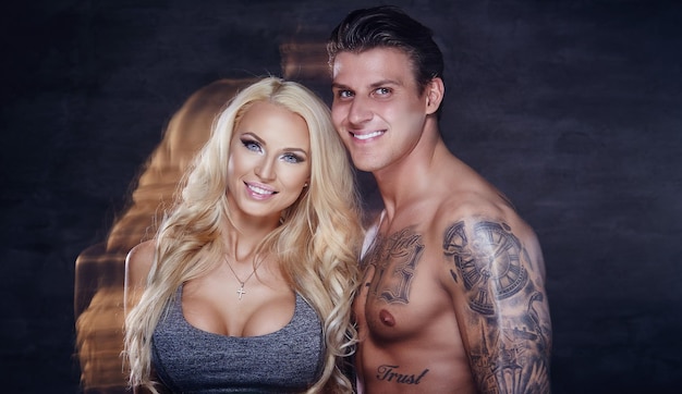 Couple de remise en forme. Homme musclé tatoué et femme blonde posant en studio.