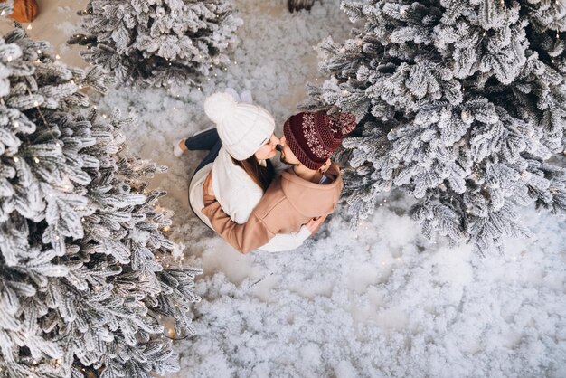 Un couple reste sur la neige dans la forêt de Noël