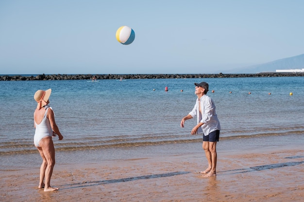 Couple de retraités jouant au ballon de plage sur la plage lors d'une journée ensoleillée