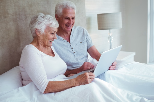 Couple de retraités utilisant un ordinateur portable assis sur son lit