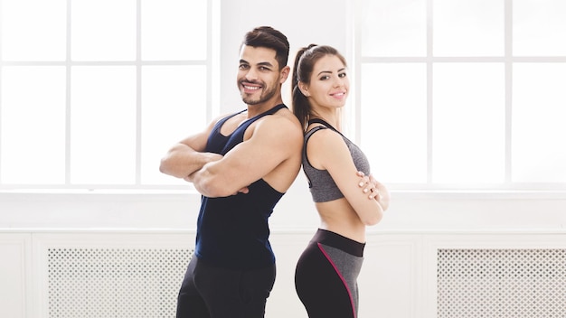 Couple réussi dos à dos et souriant en studio avec grandes fenêtres, panorama, espace libre