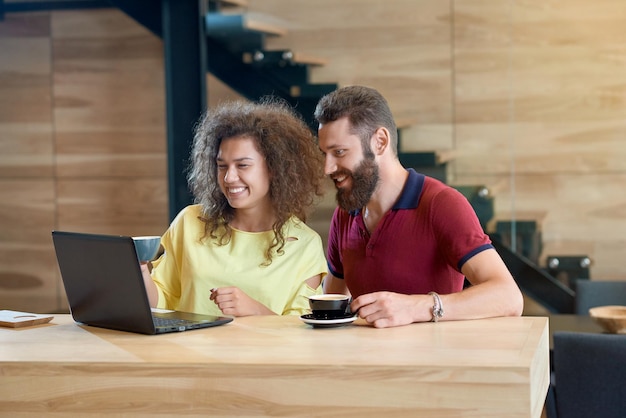 Couple riant à l'aide d'un ordinateur portable, boire du café assis dans un café