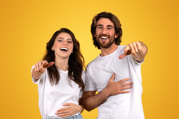 Un couple riant pointant directement vers la caméra avec une main sur le cœur partageant un moment de joie