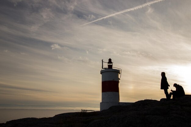 Photo couple sur le rocher contre le phare au coucher du soleil