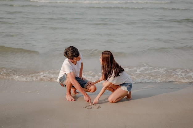 Couple romantique assis et écrit sur le sable à la plage au coucher du soleil. planifier l'assurance-vie au futur concept. couple, amour, plage, romantique, été, concept de style de vie.