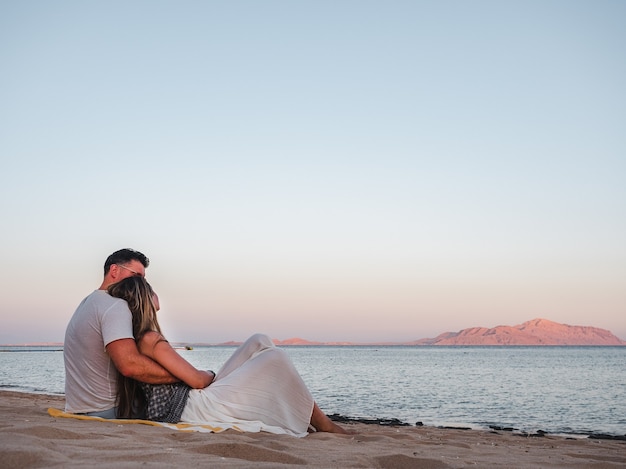 couple romantique assis sur la plage et regardant la mer