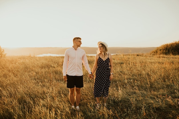 Couple romantique au chapeau marchant dans la prairie.