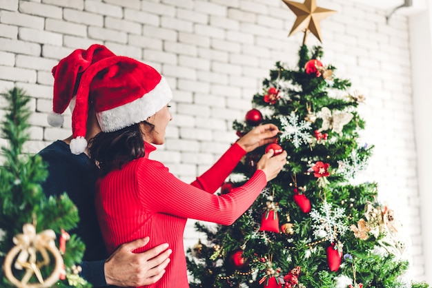 Couple romantique avec chapeaux de santa s'amusant à décorer un arbre de Noël et souriant tout en célébrant le nouvel an