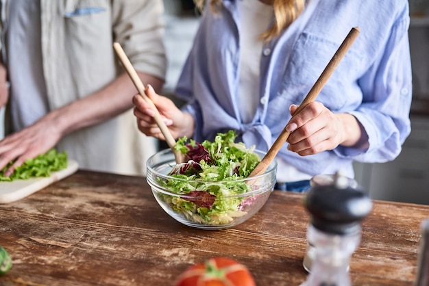 Un couple romantique cuisine dans la cuisine. Un bel homme et une jeune femme séduisante s'amusent ensemble en faisant de la salade. Concept de mode de vie sain.