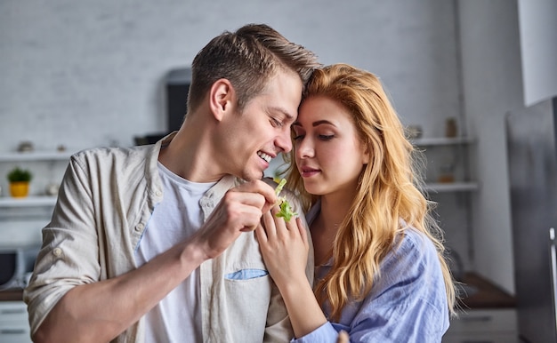 Un couple romantique cuisine dans la cuisine. Un bel homme et une jeune femme séduisante s'amusent ensemble en faisant de la salade. Concept de mode de vie sain.