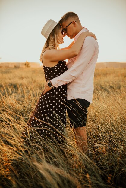 Couple romantique dans un chapeau câlin et s'embrasser dans les hautes herbes du pré.