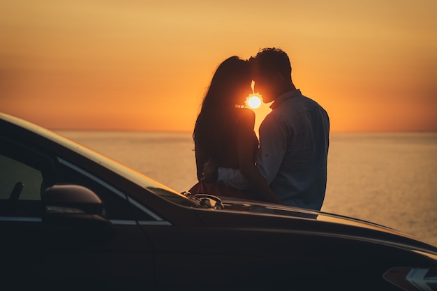 Le couple romantique debout près de la voiture sur le magnifique fond de coucher de soleil