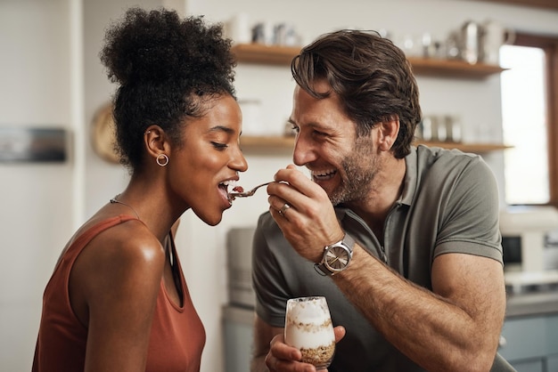 Photo couple romantique heureux et interracial mangeant un yaourt sain ensemble dans une jolie romance de cuisine douce et amusante amoureux amoureux et mari excité nourrissant sa belle femme afro délicieux dessert
