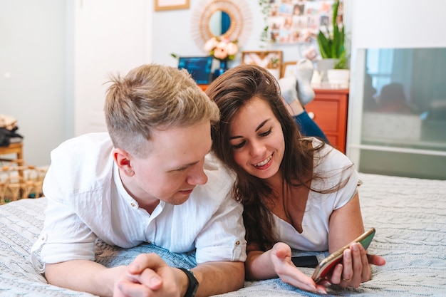 Un couple s'allonge sur un lit à la maison et communique par liaison vidéo avec des parents à l'aide d'un smartphone