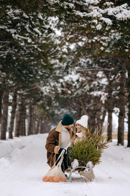 Un couple s'amusant avec un traîneau dans une forêt d'arbres de Noël, mangeant des mandarines et profitant d'une neige