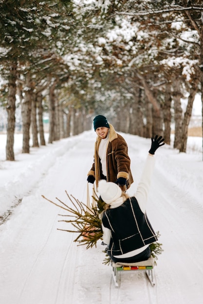 Un couple s'amusant avec un traîneau dans une forêt d'arbres de Noël, mangeant des mandarines et profitant d'une neige