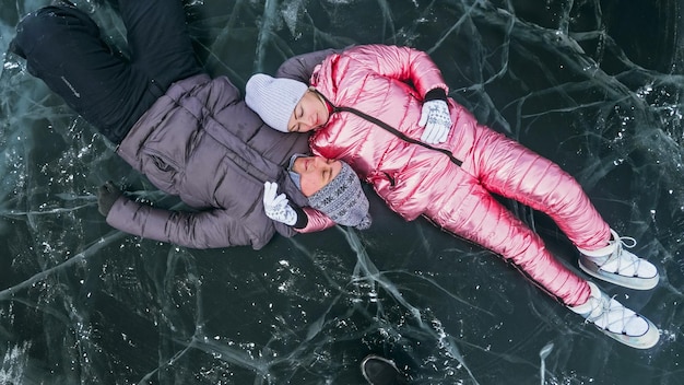 Un couple s'amuse à marcher en hiver sur fond de glace d'un lac gelé Les amoureux s'allongent sur une glace claire avec des fissures s'amusent à s'embrasser et à s'embrasser