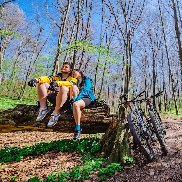 Un couple s'assoit sur une souche se reposant après avoir fait du vélo en forêt