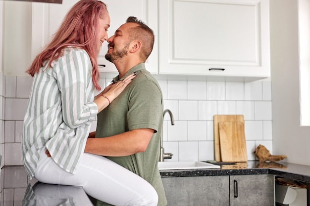 Couple s'embrassant dans la cuisine avec intérieur lumineux loft, moment romantique, week-end, en vêtements domestiques
