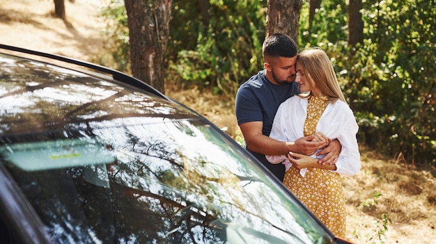 Couple s'embrassant dans la forêt près d'une voiture moderne.