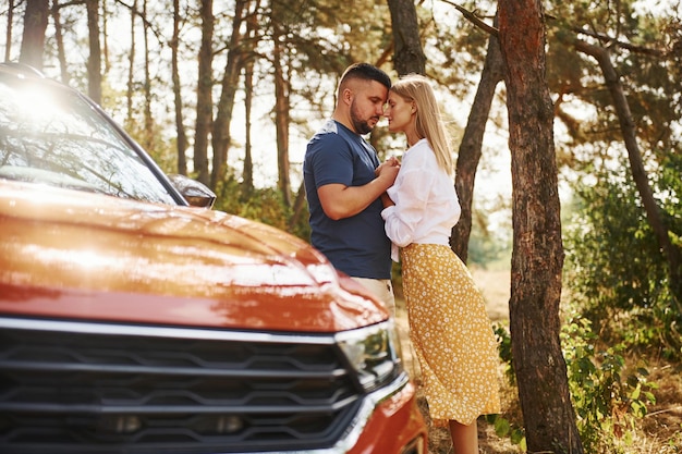 Couple s'embrassant dans la forêt près d'une voiture moderne.