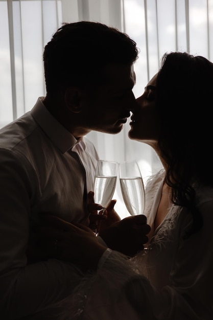 Un couple s'embrassant devant une fenêtre avec une coupe de champagne.