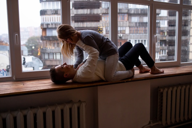 Couple s'embrassant et s'amusant dans leur chambre près de la fenêtre, un mec tenant sa belle fille bien-aimée dans ses bras