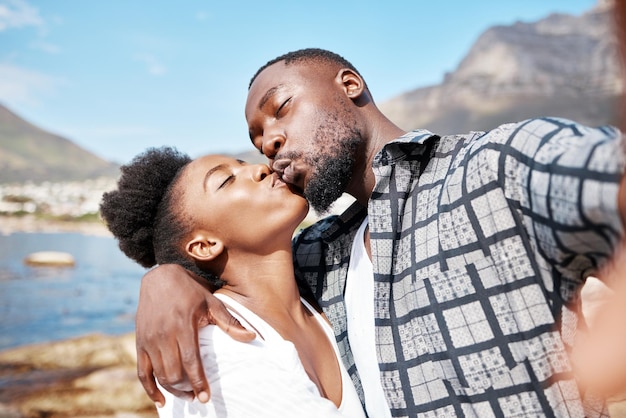 Couple s'embrasser dans un selfie à la plage en été pour le publier sur les réseaux sociaux par une journée ensoleillée dans la nature ensemble Voyager l'amour et la femme noire embrasser son petit ami africain dans un portrait de l'océan en vacances