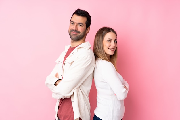 Couple en Saint Valentin sur mur rose isolé en gardant les bras croisés en position latérale tout en souriant