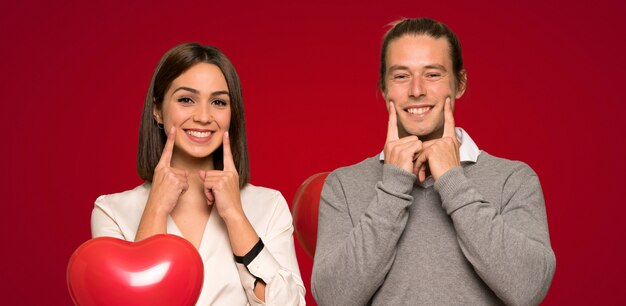 Couple en Saint Valentin souriant avec une expression heureuse et agréable sur fond rouge