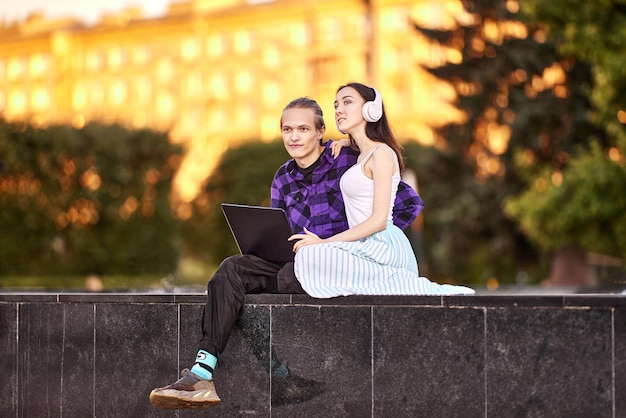 Un couple se repose dans un parc public avec un ordinateur portable et des écouteurs sans fil