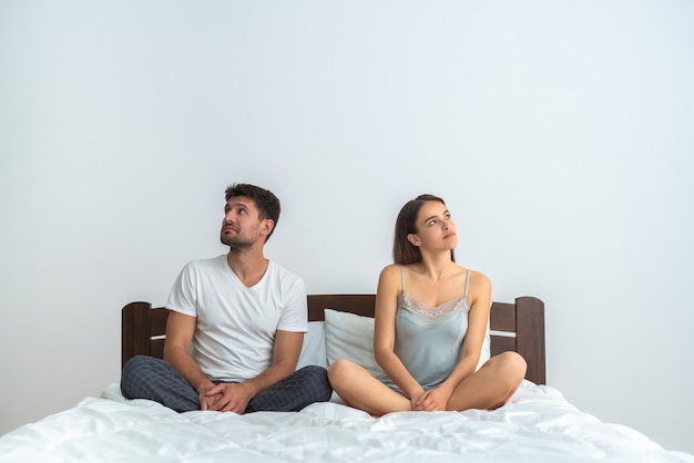 Le couple séduisant assis sur le lit sur fond blanc