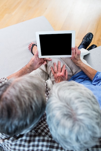 Photo couple senior à l'aide d'une tablette numérique sur un canapé