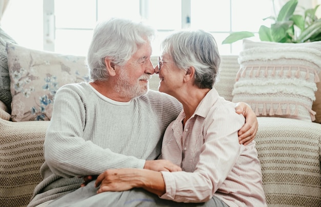 Couple senior caucasien détendu assis sur le sol à la maison se serrant nez à nez se regardant dans les yeux