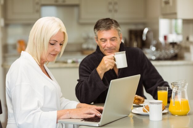 Couple senior, petit déjeuner, ensemble, femme, utilisation, ordinateur portable