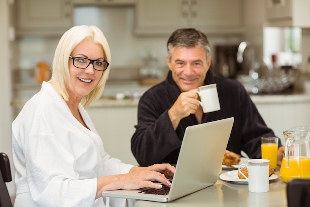Couple senior, petit déjeuner, ensemble, femme, utilisation, ordinateur portable