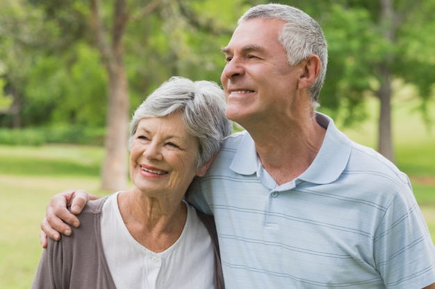 Couple senior souriant avec les bras autour du parc