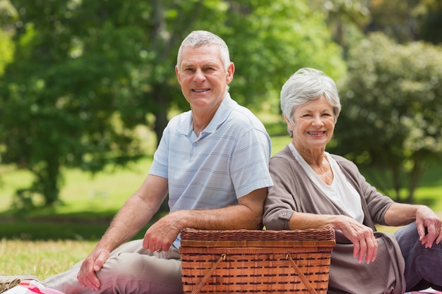 Couple senior souriant avec panier pique-nique au parc