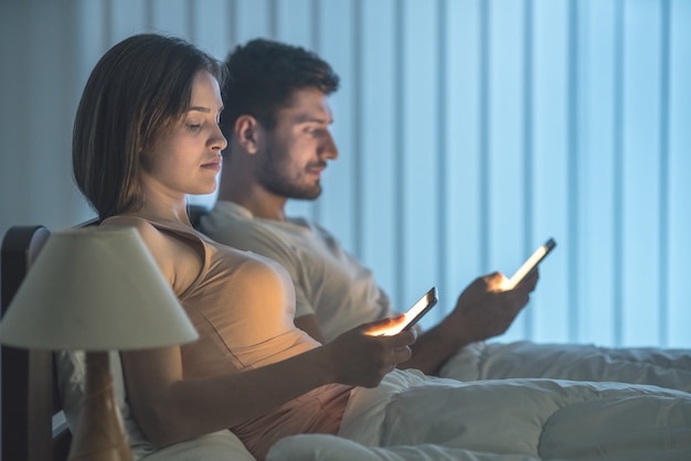 Le couple sérieux s'assoit sur le lit et téléphone