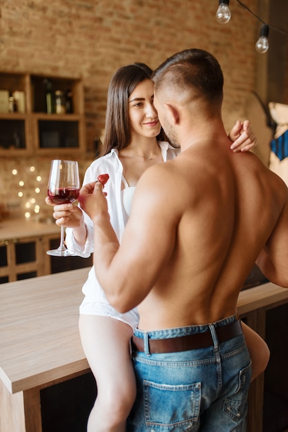 Couple sexy s'embrassant sur le comptoir de la cuisine, dîner romantique. Homme et femme préparant le petit déjeuner à la maison, préparation des aliments avec des éléments d'érotisme