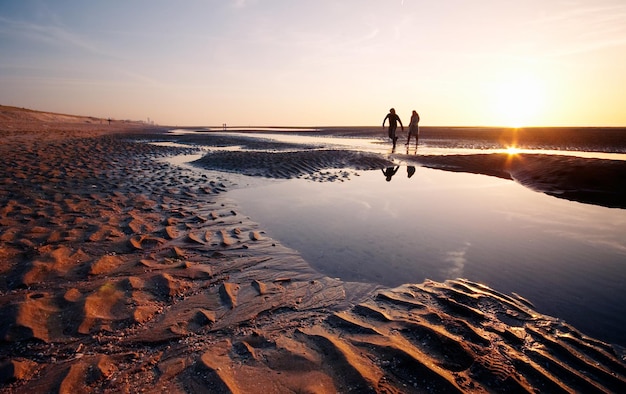 Un couple en silhouette se promène sur la plage.