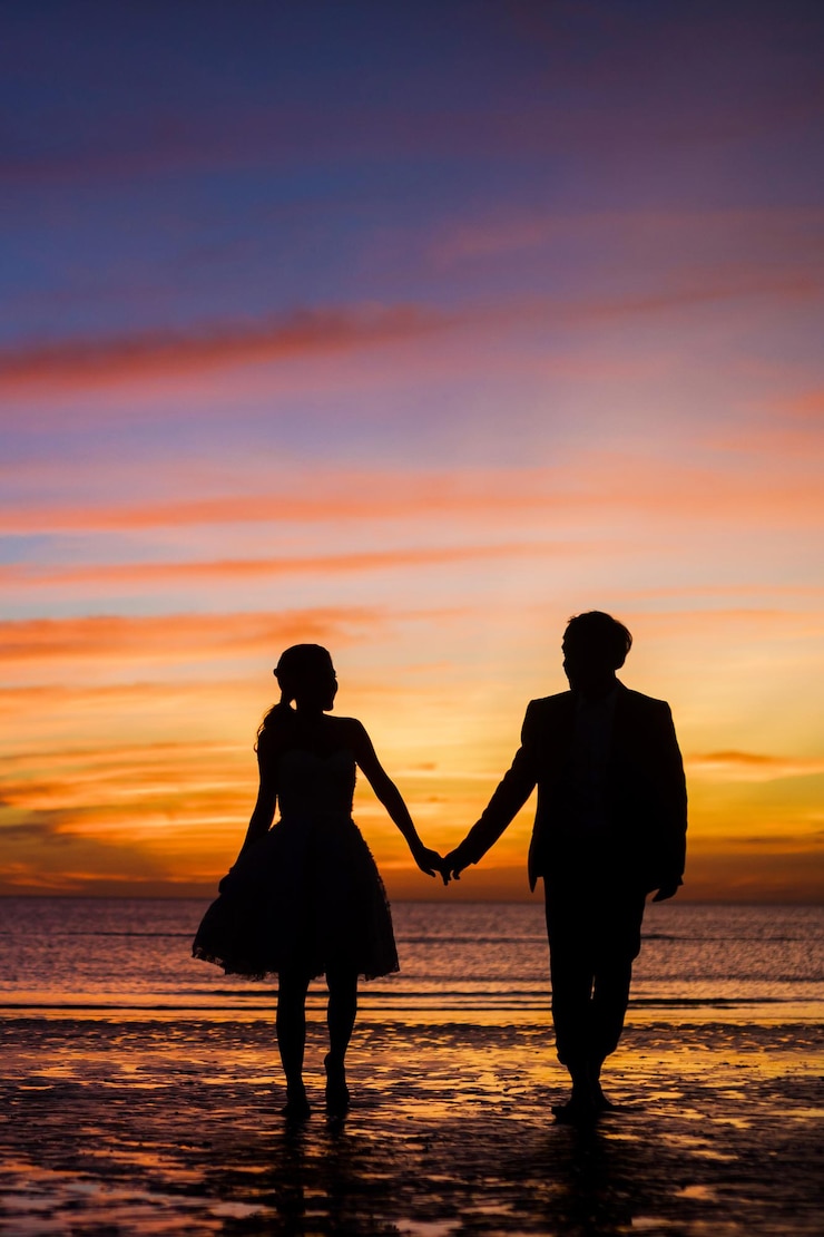 Photo un couple de silhouettes debout sur la plage contre un ciel orange