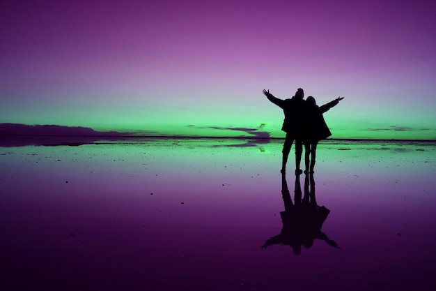 Photo un couple de silhouettes debout sur le rivage contre la mer au coucher du soleil