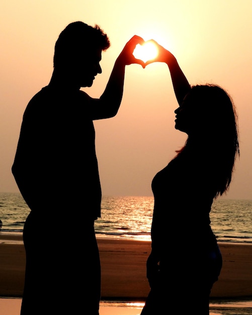 Photo un couple de silhouettes formant une forme de cœur contre le ciel au coucher du soleil