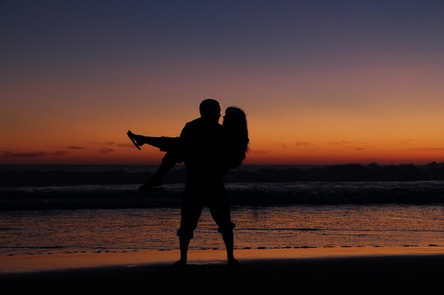 Un couple de silhouettes sur la plage contre un ciel orange au coucher du soleil