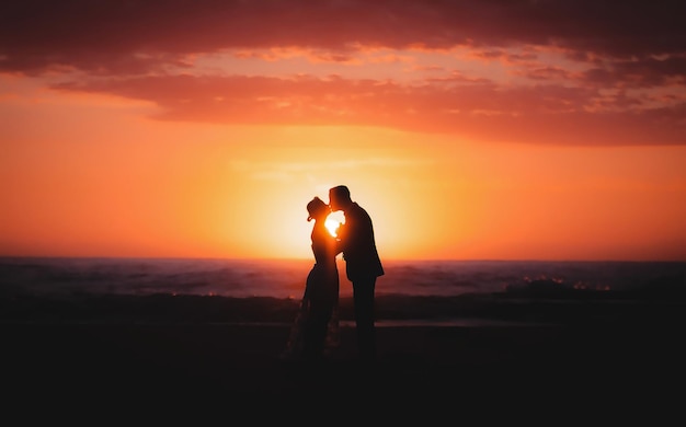 Un couple de silhouettes s'embrassant sur une falaise debout contre le ciel orange au coucher du soleil